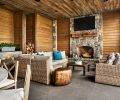 The covered outdoor living area features a stone fireplace that abuts the garage on the other side. A large, round cement table can be utilized year-round for dining outdoors thanks to built-in heaters.