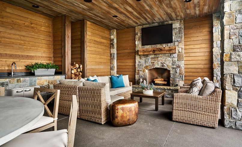 The covered outdoor living area features a stone fireplace that abuts the garage on the other side. A large, round cement table can be utilized year-round for dining outdoors thanks to built-in heaters.