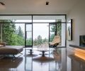 The living room is sandwiched between two walls of glass to create a spacious feel inclusive of the outdoors. A polished floor reflects thoughtfully chosen furniture.