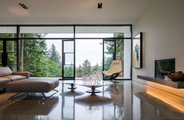 The living room is sandwiched between two walls of glass to create a spacious feel inclusive of the outdoors. A polished floor reflects thoughtfully chosen furniture.