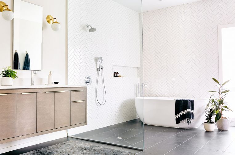 Narrow subway tile laid in a herringbone pattern brings subtle detail into the master bath. On the floor, large-format porcelain ceramic tiles from Ann Sacks offer contrast in form. The addition of brass lighting fixtures from Oregon City designer Cedar and Moss brings warmth into the space.