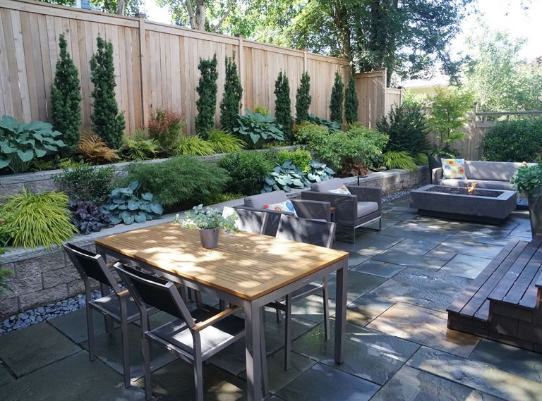 Shade-friendly foliage plants including hosta, Japanese maple, Japanese forest grass, heuchera, and Irish yew spill from terraced beds constructed from cost-effective, attractive concrete blocks. “The vertical forms of the Irish yew help break up that long fence line,” explains Tim.