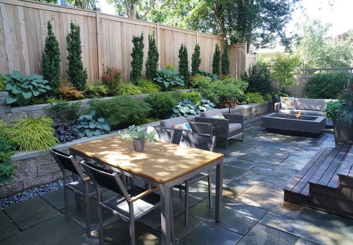 Shade-friendly foliage plants including hosta, Japanese maple, Japanese forest grass, heuchera, and Irish yew spill from terraced beds constructed from cost-effective, attractive concrete blocks. “The vertical forms of the Irish yew help break up that long fence line,” explains Tim.