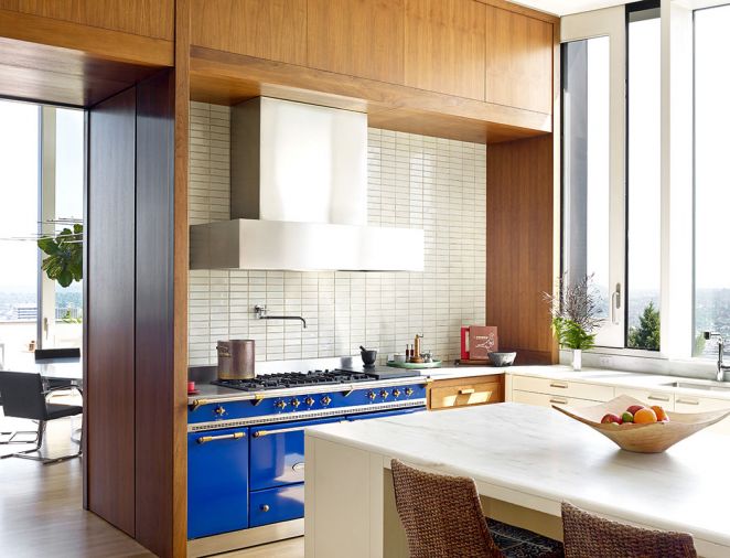 A colorful royal blue Lacanche range with five burners, adds pop to the kitchen. Stacked white pearlescent tile backsplash gets heft from a large top hat style Vent-A-Hood stainless steel hood. A waterfall edge honed Calcutta marble island countertop provides plenty of work and dining space.
Photography © Jeremy Bittermann