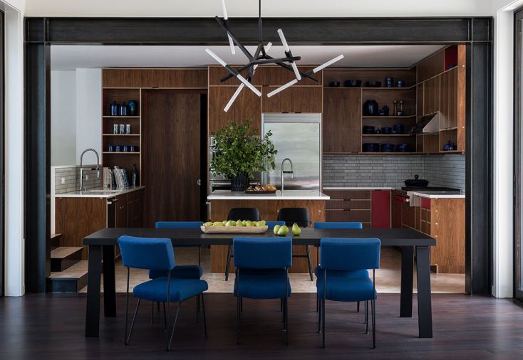 Custom walnut cabinetry from Kerf Design gives the kitchen a warm, modern feel. A few carefully placed red veneer facings on select cabinet faces, as well as a semi-hidden red jamb liner on the pocket door, provided just the right link to red in other parts of the house. “The red blends in with the walnut in a beautiful, calm way,” says Andy, “and also feels like a special bespoke detail.” The sapphire color of the ceramics collection is reflected in the dining room chairs.