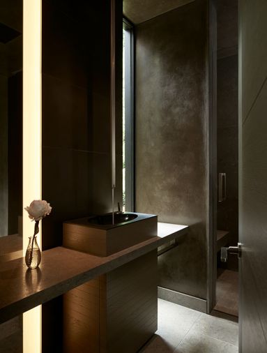 Carved black stone powder sink with Cenia Gray countertop and flooring flanks guest bedroom. Custom designed wood and metal powder room door.