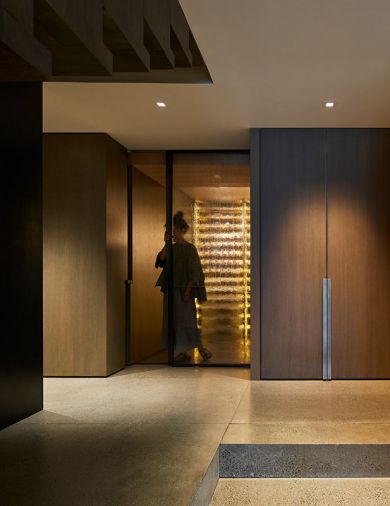 A shallow polished concrete landing with two steps down to lower level. Woman stands before glass door leading to wine cellar.