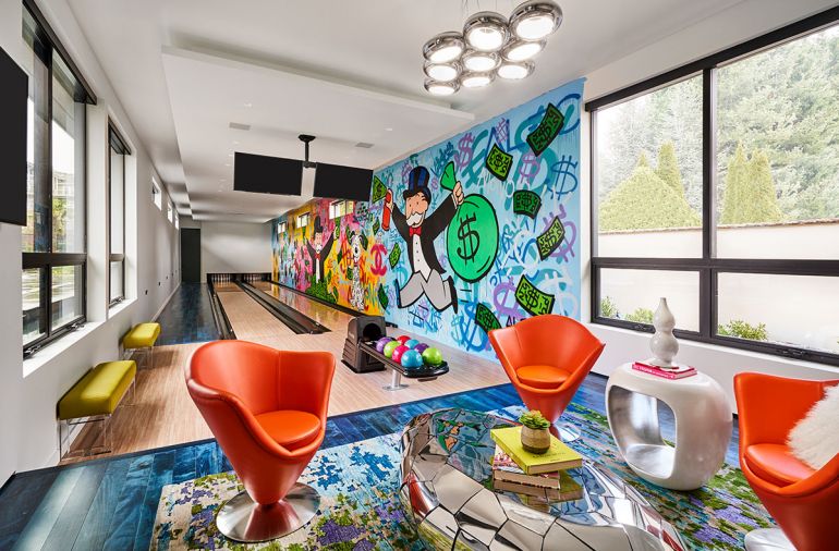 Bright blue-impregnated Provenza bowling alley flooring sets the scene for futuristic Roche Bobois orange swivel chairs, cocktail mirrored table by Phillips Collection and hand knotted rug by Kush—all teaming with “rad” Alec Monopoly graffiti mural.