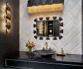 A Mirror Image black leather and brass mirror sparkles amidst the black and white themed powder room. The sculptural light fixture by Arteriors softens the geometric elements found in the Kelly Wearstler flooring and tile wall by Ann Sacks.