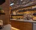 Behind the kitchen, a floor-to-ceiling stone wall peeks out from above a half-wall dividing the main kitchen from a butler’s pantry.