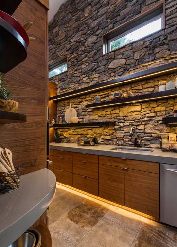 Behind the kitchen, a floor-to-ceiling stone wall peeks out from above a half-wall dividing the main kitchen from a butler’s pantry.