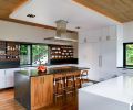 This kitchen was built for entertaining, with an open layout and plenty of space for cooking, hosting, and socializing. Dark soapstone counters contrast with white laminate cabinets and walnut accents, with oak flooring and a stained Western red cedar ceiling to match the exterior of the home. The oven, microwave, refrigerator, and dishwasher are from Miele, while the cooktop is from Monogram. A Blanco sink is finished with a KWC Luna faucet.