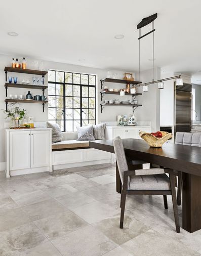 The family’s dining area got cozier with the addition of a window seat centered beneath a steel window and flanked by a pair of built-in white cabinets crowned with a pair of triple-bracketed shelves in a space once occupied by an oversized refrigerator. Adjustable Holtkötter lighting over table.