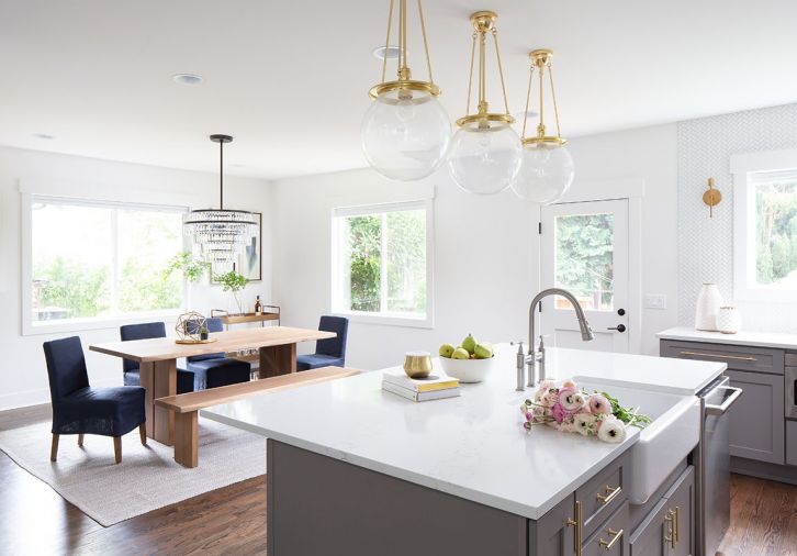 DINING A live-edge dining table and benches are paired with navy chairs, gold accessories, and a black-and-crystal chandelier, complementing the metallic threads in the room’s West Elm area rug.  SINK + HARDWARE A matte silver faucet lends a traditional element to the rectangle-shaped sink from Kohler, while a trio of globe pendants done in gold from West Elm are suspended above.