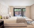 The master bedroom is a serene retreat overlooking a private patio, with a bed and nightstands from Restoration Hardware, Schumacher benches covered in Townsend Leather, and light-colored accessories from Room & Board, Village Interiors, Rubelli, C&C Milano, rug from Stacey Logan.