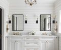 The master bathroom and powder room tie in multiple elements from the home, including marble countertops, black-framed mirrors and glass shower door that imitate the windows found elsewhere, shiplap walls, and brushed-brass hardware and fixtures. A cloudlike gray and white wallpaper in the powder room backs the client’s own vintage pine dresser repurposed into a vanity, with wall-mounted faucet and an antique mirror to round out the look.