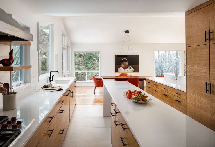 White oak casegoods make a statement in the kitchen, where an elongated island provides storage, acts as a serving buffet, and allows stools to tuck under for easy circulation. Matte black fixtures, hardware, and furnishings are both a punctuating statement and long-lasting neutral. In the dining room, a Design Within Reach geometric pendant that coordinates with the client’s Sally Haley painting hangs over a large walnut table.