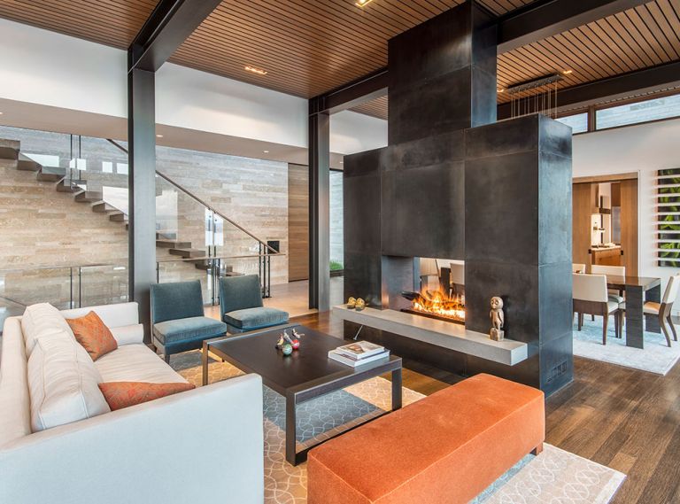 A cantilevered staircase with glass railing sits against interior/exterior envelope of Amber Rose flame cut stone contrasting with cold rolled blackened steel fireplace. Gregorious|Pineo Battista dining table; Holly Hunt chairs; blown/cast glass Trinh Nguyen artwork. Photo © Derek Reeves