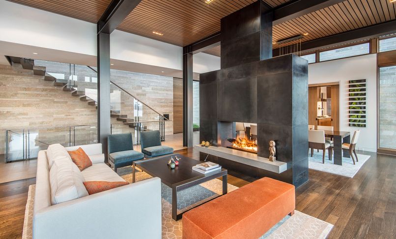 A cantilevered staircase with glass railing sits against interior/exterior envelope of Amber Rose flame cut stone contrasting with cold rolled blackened steel fireplace. Gregorious|Pineo Battista dining table; Holly Hunt chairs; blown/cast glass Trinh Nguyen artwork. Photo © Derek Reeves