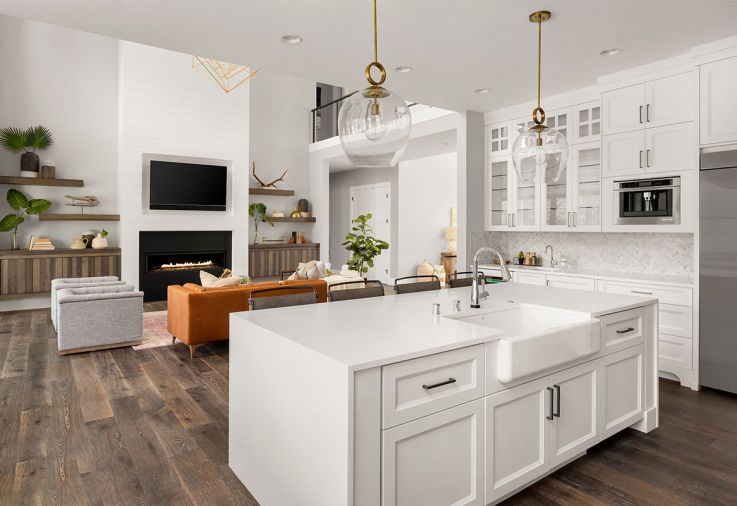 Custom white cabinets in the beverage area designed by Hayes Cabinets feature a glass front that adds to the space’s airy vibe and showcases glassware and white dishes. In the adjacent great room, the modern rectangular fireplace, designed by Axiom, has a black iron tone cohesive with the other finishes in the home.