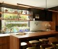 Solid walnut island with Restoration Hardware stools for casual dining. South-facing windows feature custom hanging walnut shelves with blackened steel hangers and laser cut custom wine glass racks mounted to shelving’s underside.