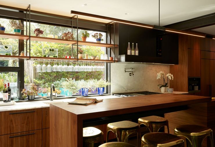 Solid walnut island with Restoration Hardware stools for casual dining. South-facing windows feature custom hanging walnut shelves with blackened steel hangers and laser cut custom wine glass racks mounted to shelving’s underside.