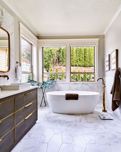 Elongated hex tile by Z Collection runs across the floor and up the half-wall that envelopes the Fleurco Aria Voce Petite tub. Standing brass Delta Trinsic tub filler echoes the inlays found throughout the home’s cabinetry.