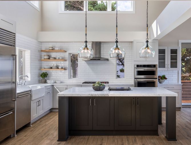 The kitchen and dining room’s airy vibe comes thanks to its two-story space and abundant windows. Kitchen cabinetry is a combination of lighter gray on the perimeter and a darker blue-gray hue for the island cabinets. Soft white honed Carrara marble countertops complements tile that mimics the movement of waves. “This all adds lightness and reduces the weightiness of the home on its occupants,” explains homeowner Selma Pierce.