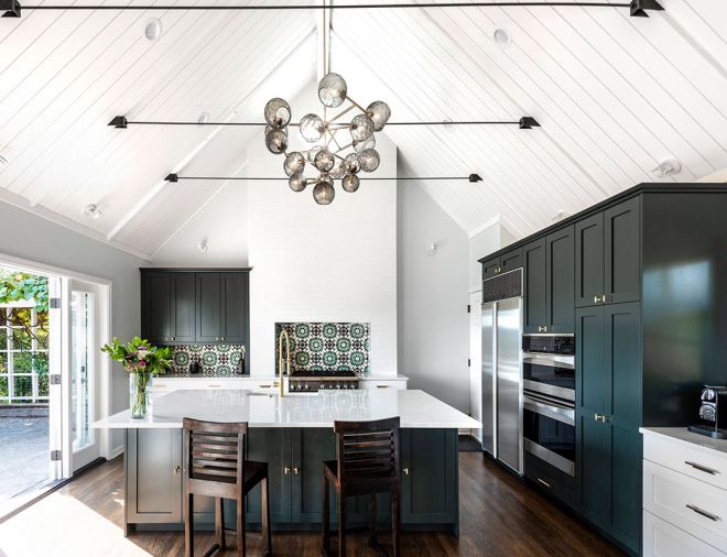 French doors connect the kitchen to the home’s yard and patio, linking the indoor and outdoor spaces and enhancing the open, airy feel created by the high ceilings. Custom cabinets were trimmed out to resemble furniture, then painted in Farrow & Ball Studio Green. The dark color adds a sense of drama to the otherwise light, bright space.  Jeff chose quartz for the countertops for its durability and clean, understated look. The backsplash is custom tile from Cement Tile Shop, laid in a graphic geometric pattern.