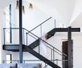 An open steel frame staircase with oak treads echo the home’s wide plank European oak flooring. Large Loewen windows bath the staircase in light along with a trio of Finnish Secto pendants. Artiss’s own slab ceramic box on paired black and white oak Josh Vogel coffee tables.