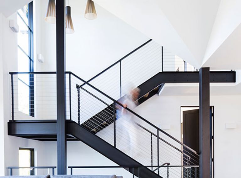 An open steel frame staircase with oak treads echo the home’s wide plank European oak flooring. Large Loewen windows bath the staircase in light along with a trio of Finnish Secto pendants. Artiss’s own slab ceramic box on paired black and white oak Josh Vogel coffee tables.