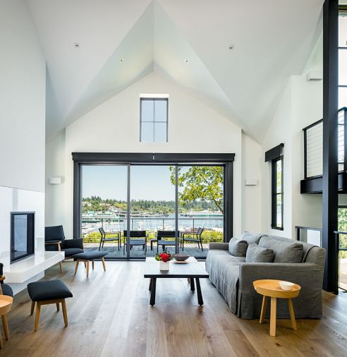 La Cantina sliding doors that overlook WA State Ferry Dock are framed beneath 15' ceiling rising to apex of one of its cross gabled roofs. Embrace Chairs by Carl Hansen/Austrian trio EOOS flank the Crystal White marble fireplace surround. Danish Muuto side tables.
