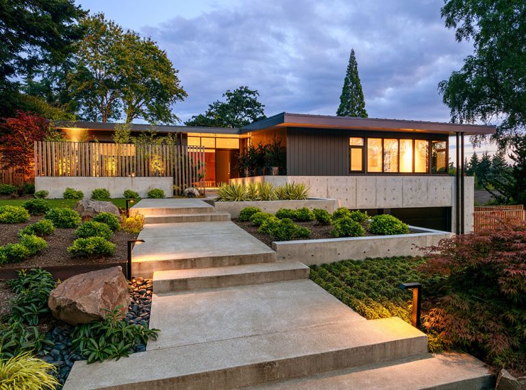 Williams’ architectural design lends new importance to the master by placing it above the garage now tucked out of sight below. Privacy comes from a wraparound concrete balcony. Shapiro Ryan’s wide concrete walkway rises elegantly through the graduated, terraced minimalist landscape, with grass eye-break before Williams’ wood and steel fencing perched atop concrete.