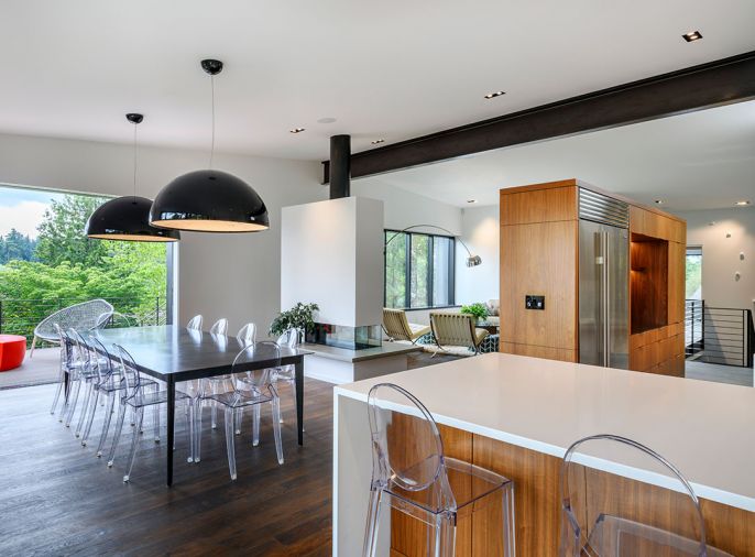 Working from the clients’ desire for light and airy feel inside and out, Williams’ open floor plan is punctuated by an exposed, blackened steel beam traversing the slightly sloping metal roof. A concrete hearth on the double-sided Ortal Space Creator fireplace echoes the use of modernist poured-in-place material. Stained oak flooring grounds the American Black Walnut island and refrigerator cabinetry. Staircase leads downward to garage. Living room Quantum windows feature Triple-Black stained mahogany interiors.