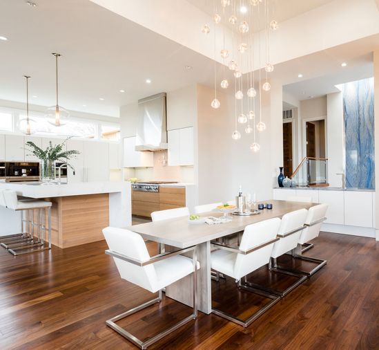 Floor-to-skylight Azul Macaubus polished quartz lining entry staircase is echoed on dining room cabinet countertops. Misu by Terzani chandelier adds sparkle to high ceilings. Dark walnut flooring grounds the open plan.