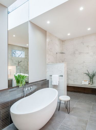 Oval soaking tub is grounded by 24' x 24' Vallelunga Foussana Gray porcelain tile. Kohler rain showerhead is highlighted in the left-hand shower. Back shower wall in Calcutta Momento porcelain tile in Ambra wave.