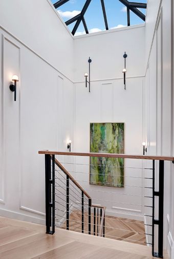 U-shaped central staircase positioned at rear of home reveals the spectacular view upon reaching top floor. Skylight capped stairwell brings in lots of light. Circa Nodes Collection stairwell sconces add linear appeal to the traditional molding reiterated in adjacent carriage house sitting room.