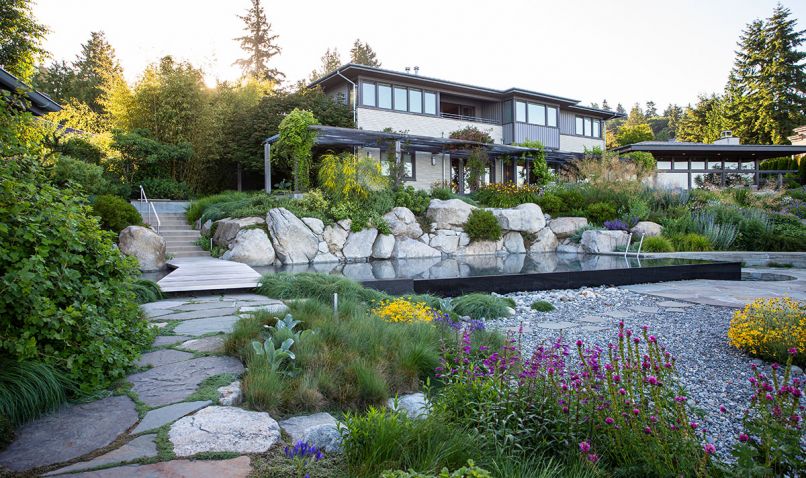 Where only lawn once sloped toward the failing bulkhead, now a black infinity pool backed by boulders and vegetation are at the heart of the family compound.