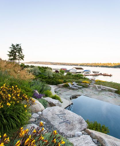 Colorful Hemerocallis “Corky” Daylily border the pool in foreground, adding splashes of color to a series of large boulders inscribed with playful advice, “Look Before You Leap.” The reiteration of circles and angles repeats from granite infinity pool edge to a wading pool that invites toddlers and adults alike to dip their feet. A circular firepit beyond can light up the night sky. A meadow of Roemer’s fescue, a native grass, references much of the endangered Puget Sound lowlands.