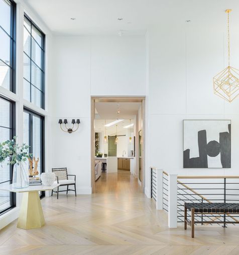 Dumont reiterates black, white, and gold palette throughout entry: painted wood paneling, steel staircase, Visual Comfort Cubist pendant, Arteriors sconces, hex-shaped table, and artwork. French doors flank Marvin aluminum clad windows.