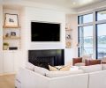 Dumont laid out the custom stained tongue and groove chevron wood flooring in entry by Salisbury Woodwork of Bainbridge Island. Shiplap wall and TV surround contrasts with waxed blackened steel fireplace and black indigo herringbone stone insert. J Redmond sectional with stone fabric faces off with pair of cognac Dorado leather-trimmed chairs from J Garner Home. White oak stained shelving echoes kitchen cabinetry. Marvin windows open to water view. Sturman’s custom walnut trimmed archways are an eye-catching detail.