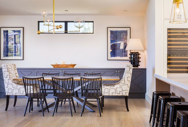 Dining room, adjacent to both kitchen and pantry on one side and living area on other, views covered deck through La Cantina multi-slide glass door. The soffit aligns with roof plane change above. Grids on custom buffet matches pattern on master walk-in closet barn door. A mix of geometric patterns, including Leathercraft host chair fabric, the Four Hands “Spider” crossed table legs and buffet doors, all from J Garner Home. Restoration Hardware chandelier.