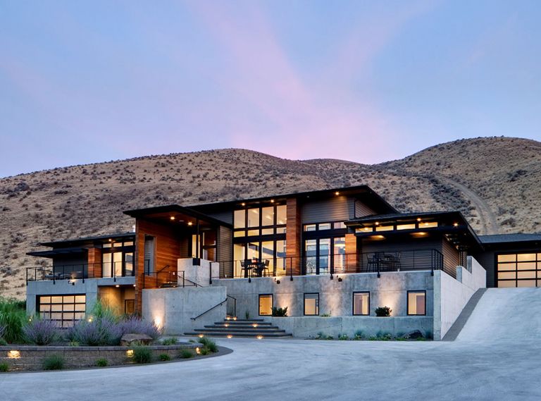 Tucked into the Badger Mountain foothills, this 5,000 sq. ft. linear Pacific Northwest modern home with Pagoda-like roof and deep overhangs sits perpendicular to the slope with expansive views in two directions. Eschewing the usual daylight basement styles found locally, architect Taylor Callaway designed a concrete and stucco basement for the blended family’s children bedrooms, then trimmed the setback main floor in clear Western Red Cedar. The entry element has switchbacks and geometric forms to make the trek more interesting.