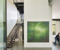 Lawrence Fodor (Friesen Gallery) oil on canvas entitled “Rain Forest” graces the entrance on a double-height foyer wall. The kitchen island is seen at right, while a sculpture features two businessmen fighting over money at left beneath the staircase rising to the second floor.