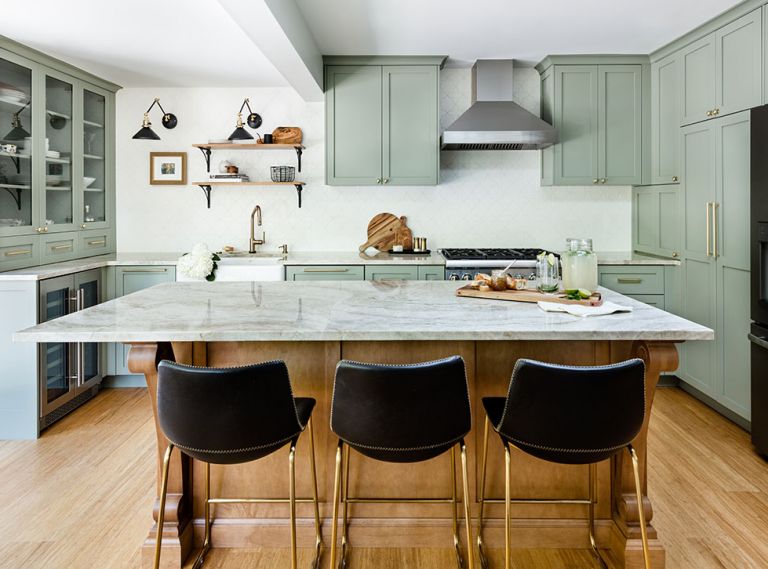 The Taj Mahal quartzite topped island is the focal point of the new kitchen while cabinets wrap around the walls before ending at a china hutch fitted with a beverage refrigerator. A beam is the only remnant of the wall that cut the kitchen in half. Designer Popov diminished the beam’s impact by dividing the wall into sink and range zones and steering the eye to shelving above the sink. Beside the refrigerator, the pantry was built around a venting pipe in a second accommodation of the home’s structural history.