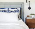 Serenity reigns in master bedroom: soft blue tufted headboard plays against geometric and blue trimmed pillows grounded by a floral bedside Joybird rug.