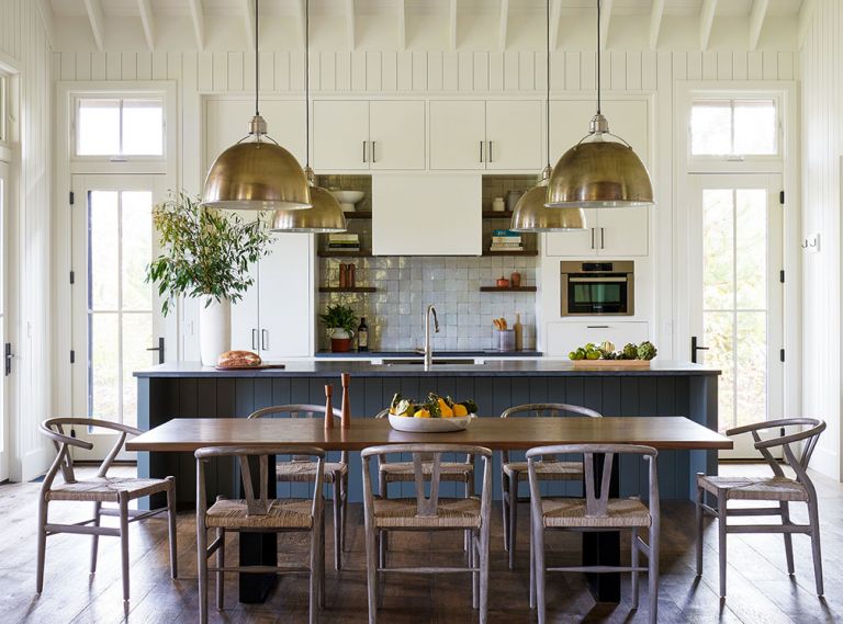 Vaulted ceilings add a sense of spaciousness to the kitchen/dining room when families gather for meals. Wire brushed wide plank oak flooring with custom finish by Natural Creations runs throughout home. Painted Benjamin Moore Gray Garden kitchen island by Traditional Woodcraft. Bosch electric cooktop with Clé Zellige backsplash tiles; freestanding custom stained oak shelving. Shiplap 1x6 walls by Windsor One. Custom hood and cabinetry: Traditional Woodcraft. Oversized Circa Lighting pendants. Custom dining table by Meyer Wells; Four Hands dining chairs.