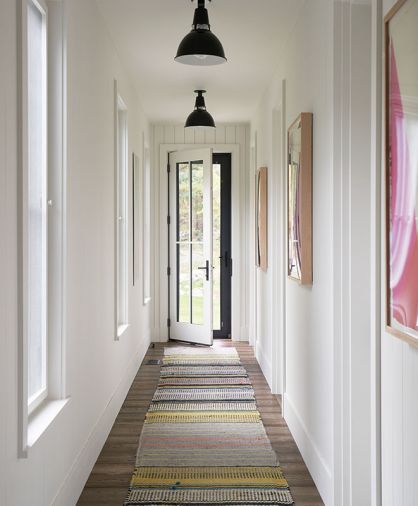 Interior designer Laura Morawitz joined thriftiness with ingenuity to create this 18' long hall rug by stitching together three colorful West Elm runners that were on sale. Black metal Circa Lighting pendants draw the eye toward the Windsor windows and door in the lengthy hallway.