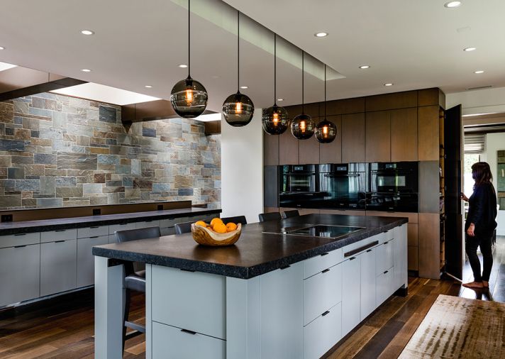 A new wall of ovens flanked by sleek wood cabinetry replaces an oft-cluttered kitchen office desk, utility closet and single oven. White oak custom stained floors by Eurocraft Hardwood Flooring tie the rooms together.