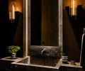 Powder wall mounted faucet by Boffi is activated by round knob at right. Vanity mirror is lit from behind as well as by the Jonathan Browning sconces.